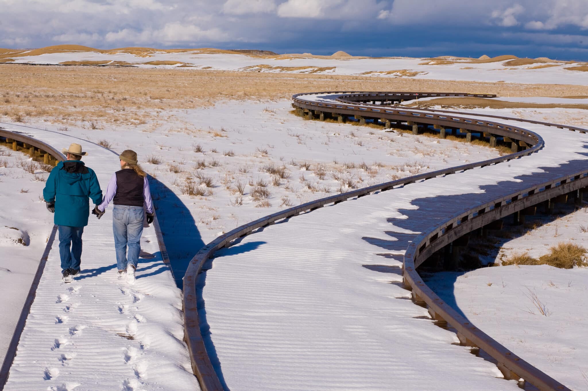 A couple walks down The Tributary, Formerly known as Huntsman Springs in Driggs, ID view from walking down the boardwalk with fresh snow on the ground.